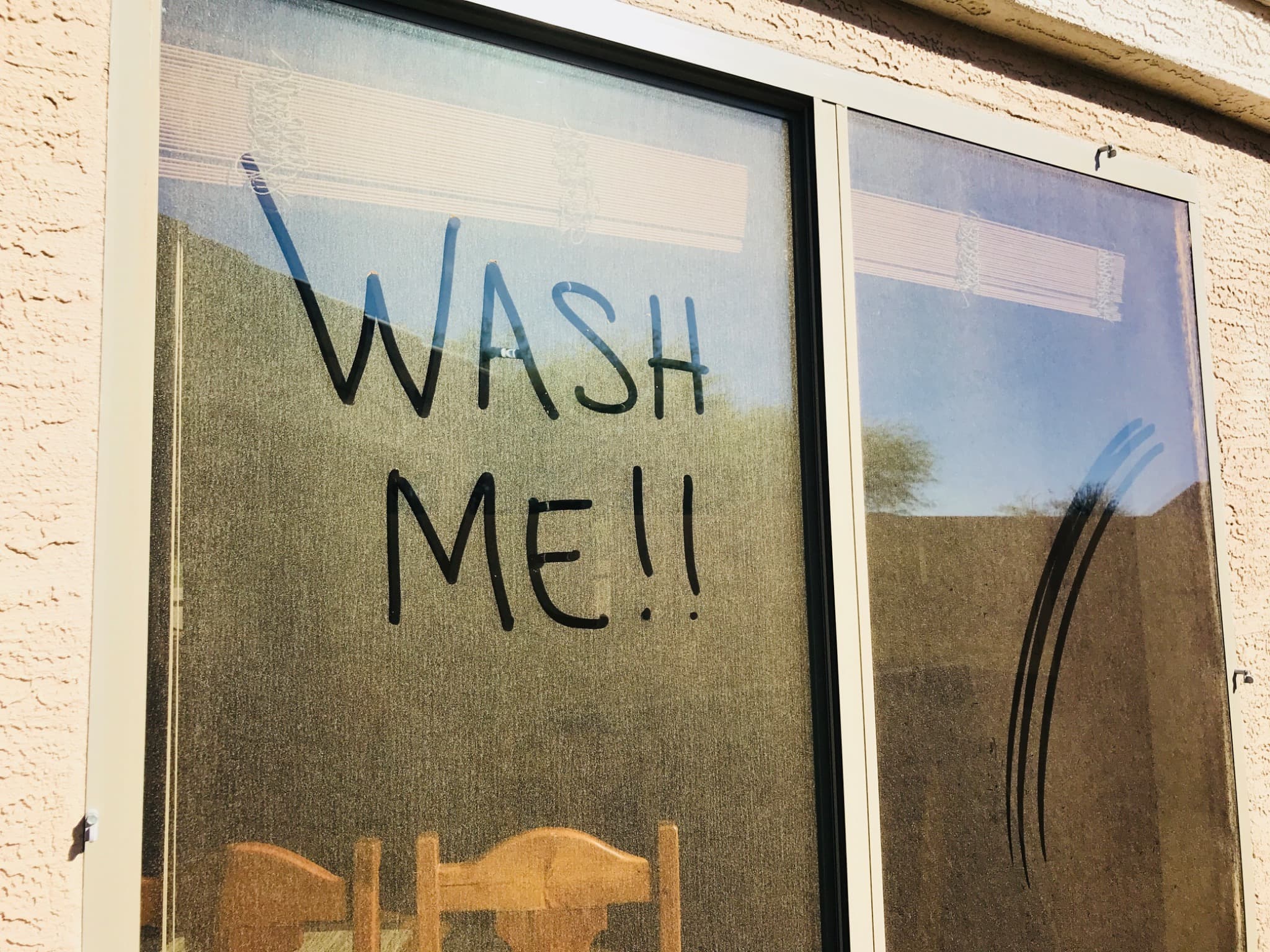 Heavily dust-coated sliding glass door with WASH ME!! finger-written in the dirt