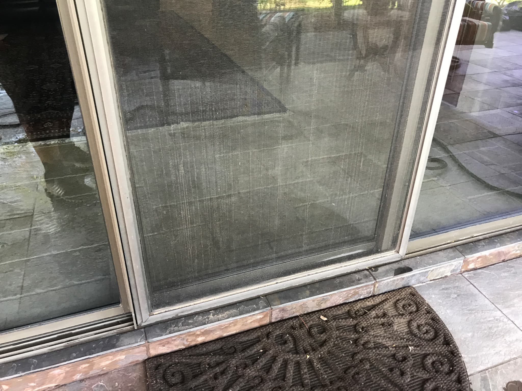 Sliding patio door and screen with dust, streaks, and buildup along the lower frame and track