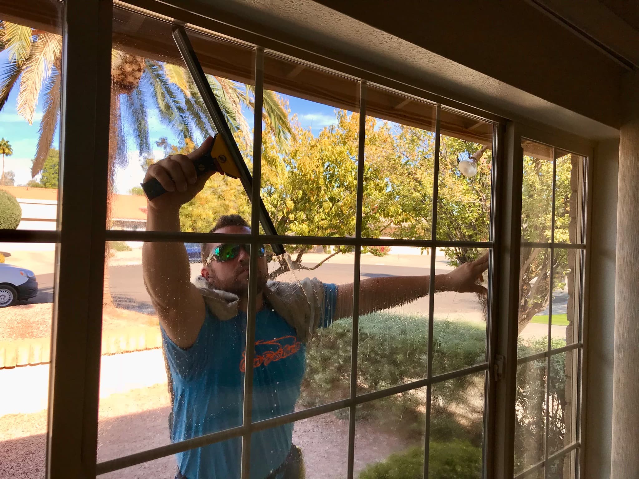 Professional window cleaner using a squeegee on a large divided residential window, viewed from inside the home