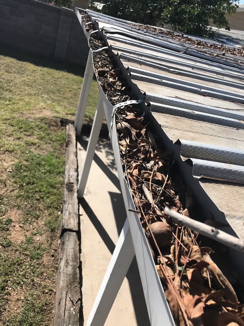 Gutter maintenance from a ladder — shingle roof and desert sky, Olsen Brothers