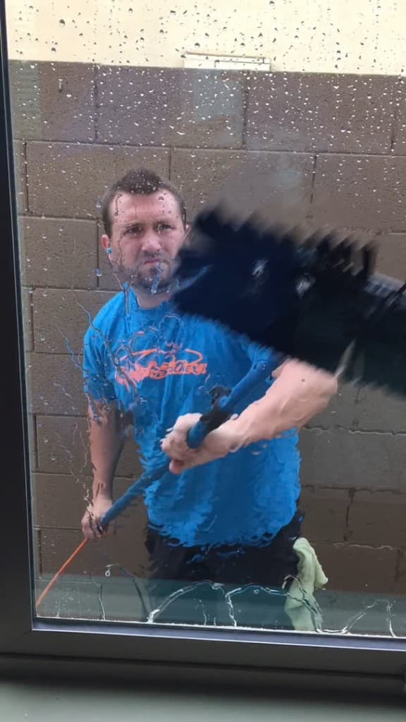 Technician cleaning exterior residential glass with a water-fed pole — soapy water on the pane, photographed from inside the home