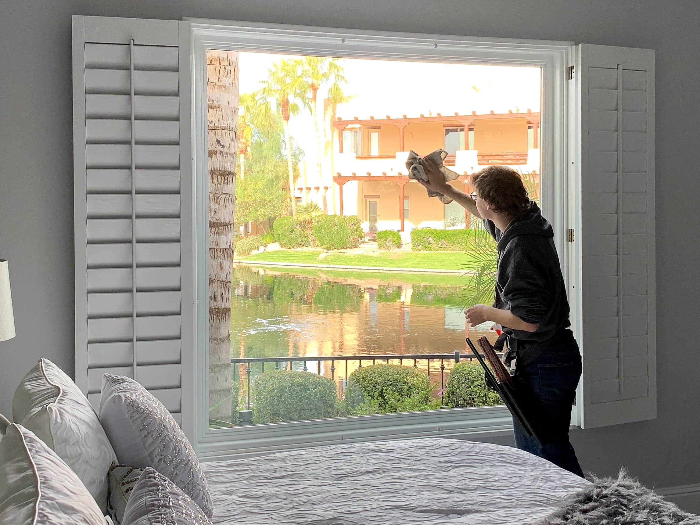 Olsen Brothers technician hand-detailing a large bedroom window with a lake view — East Valley, Arizona