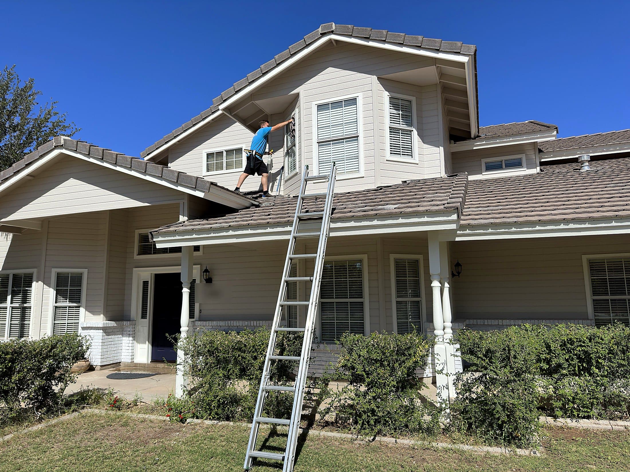 Technician cleaning second-story windows from the roof with a ladder in place — residential window cleaning, Arizona