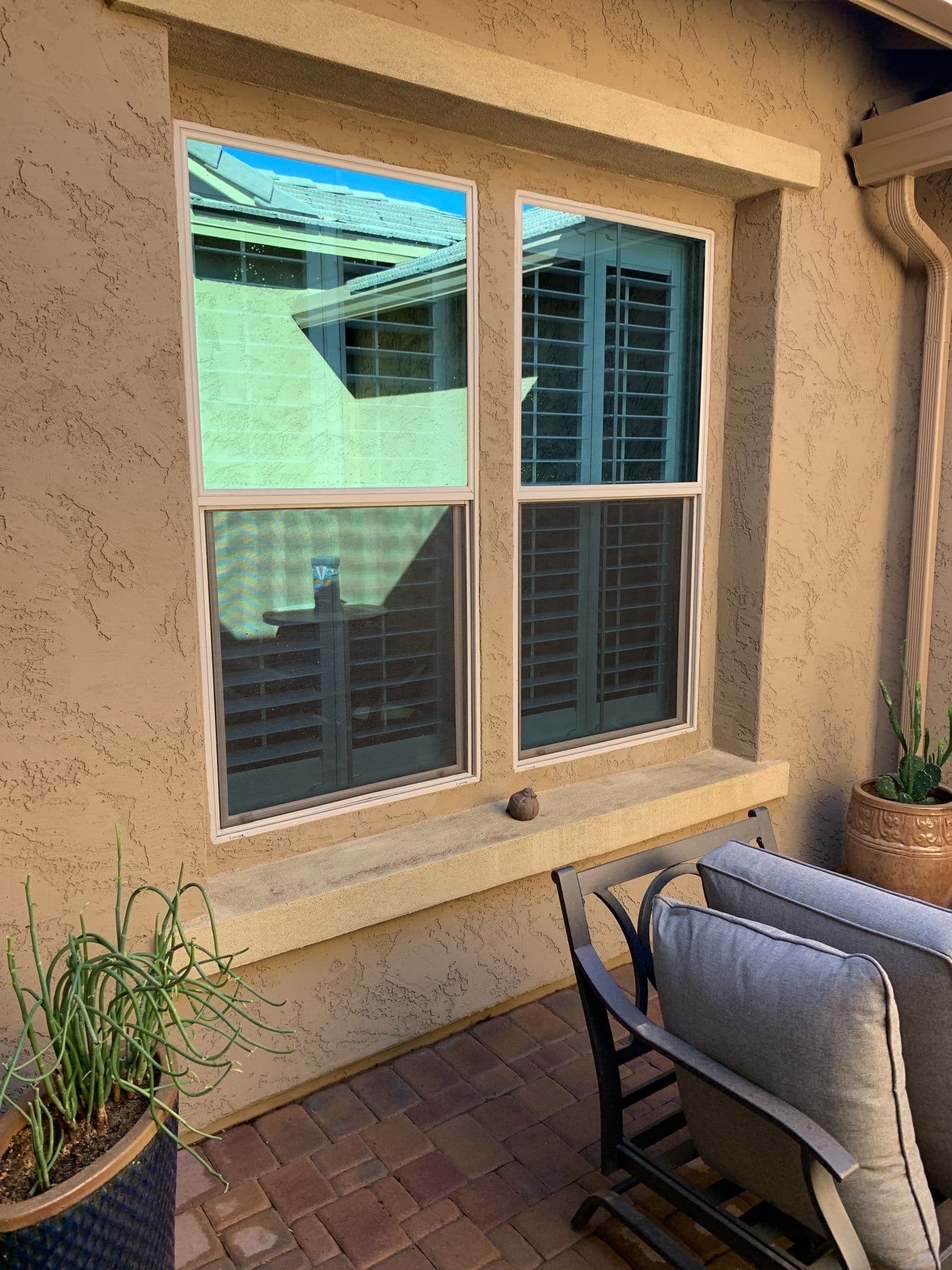 Two double-hung windows reflecting blue sky on a stucco home beside a brick patio — Eastmark