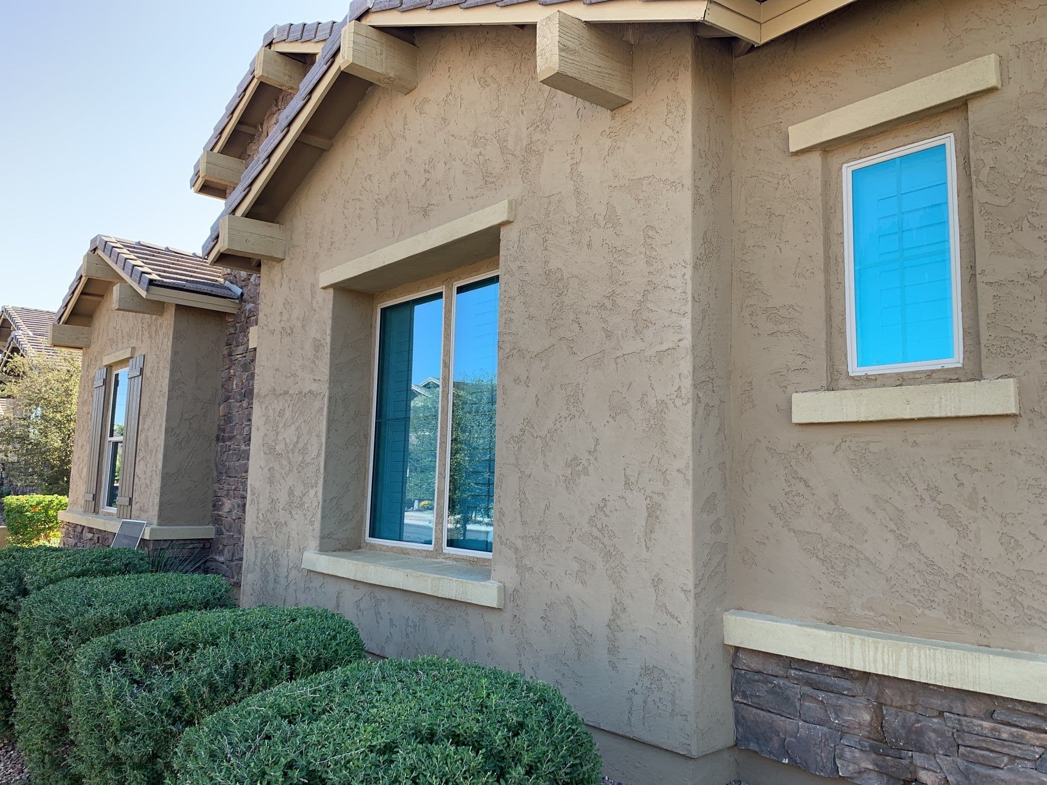 Large windows with sky reflections, stone veneer, and shrubs — Eastmark residential